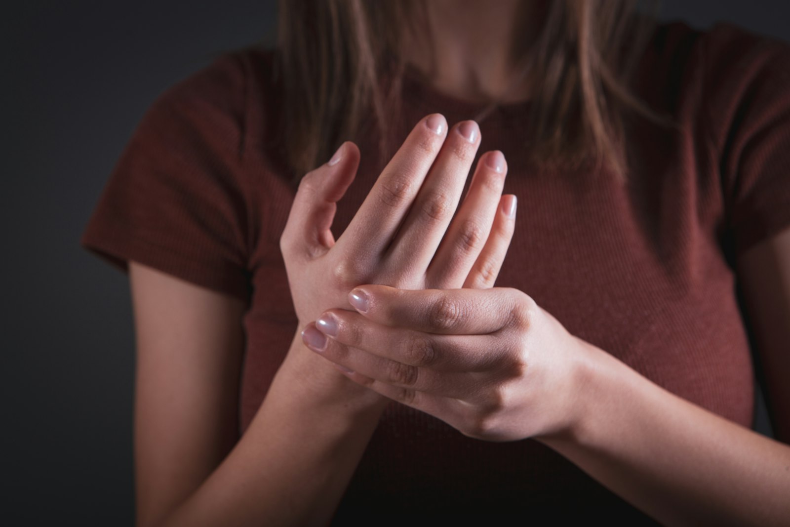A woman in a red top holding one hand in the other, as if it aches