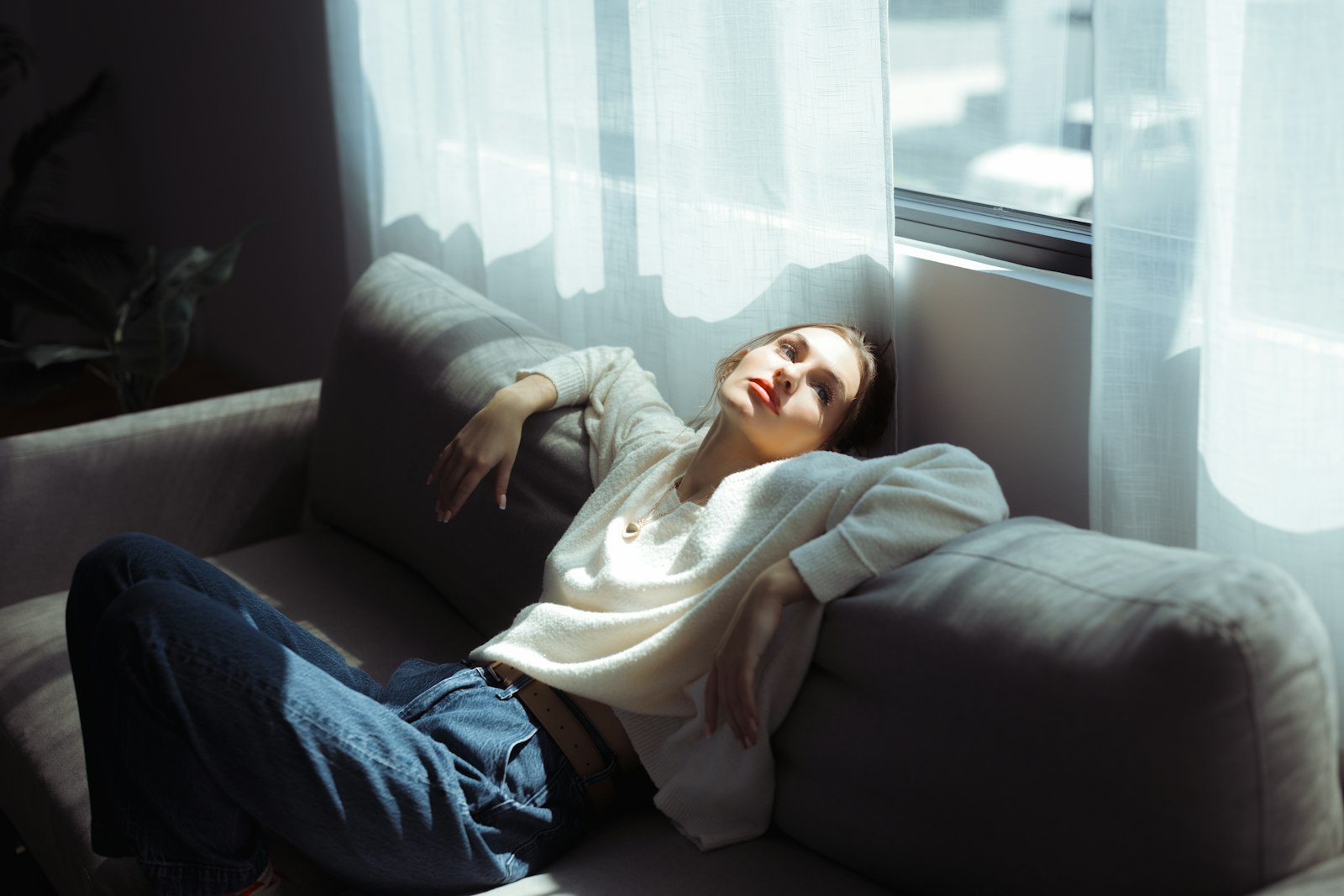 A woman in a white sweater lying back on a grey sofa in afternoon light