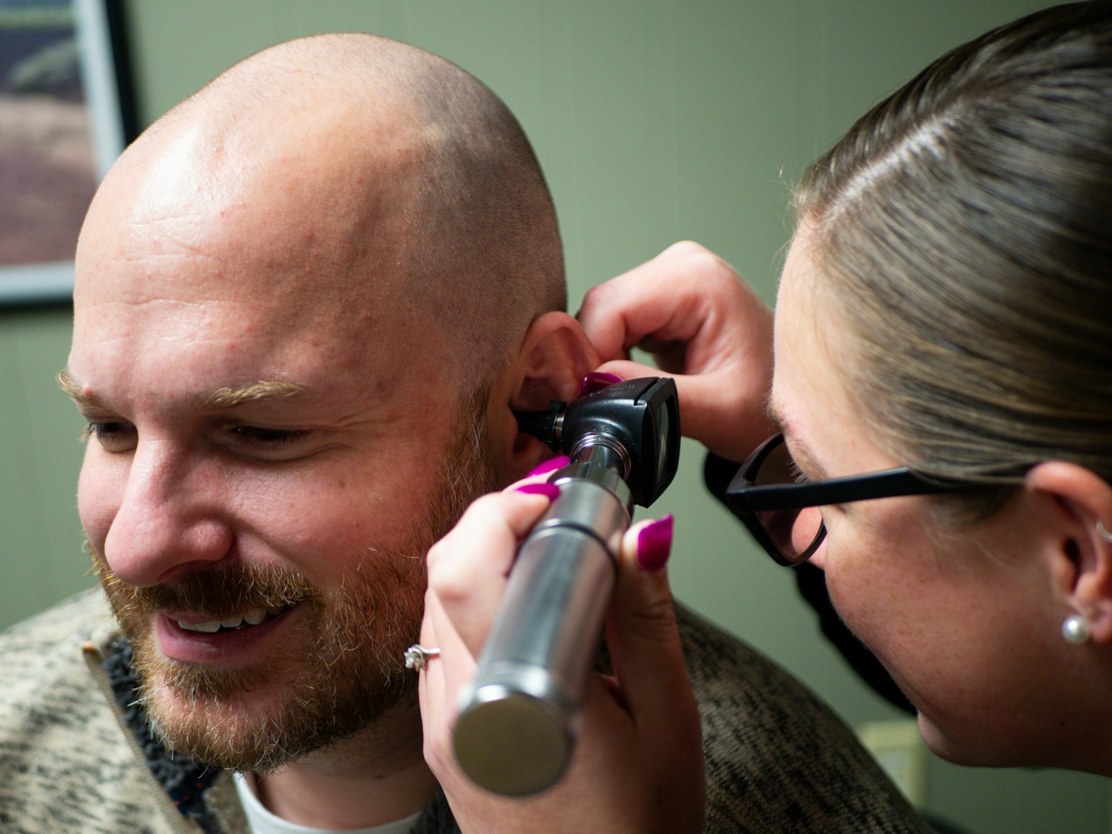 An audiologist looking into a smiling man’s ear with an otoscope