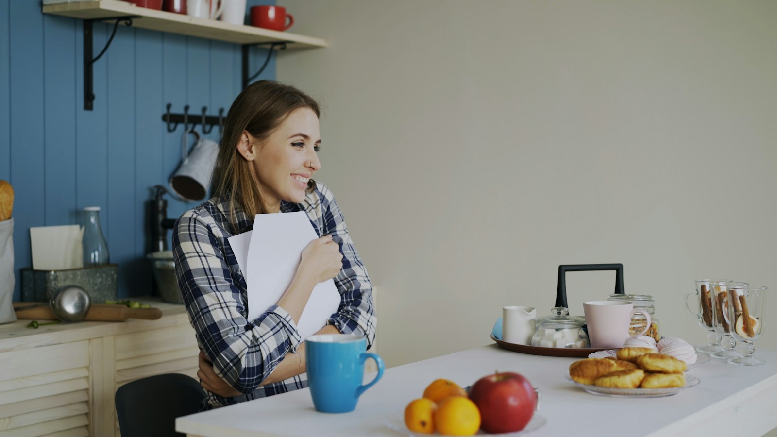 A woman at a kitchen table smiling as she holds a printed letter