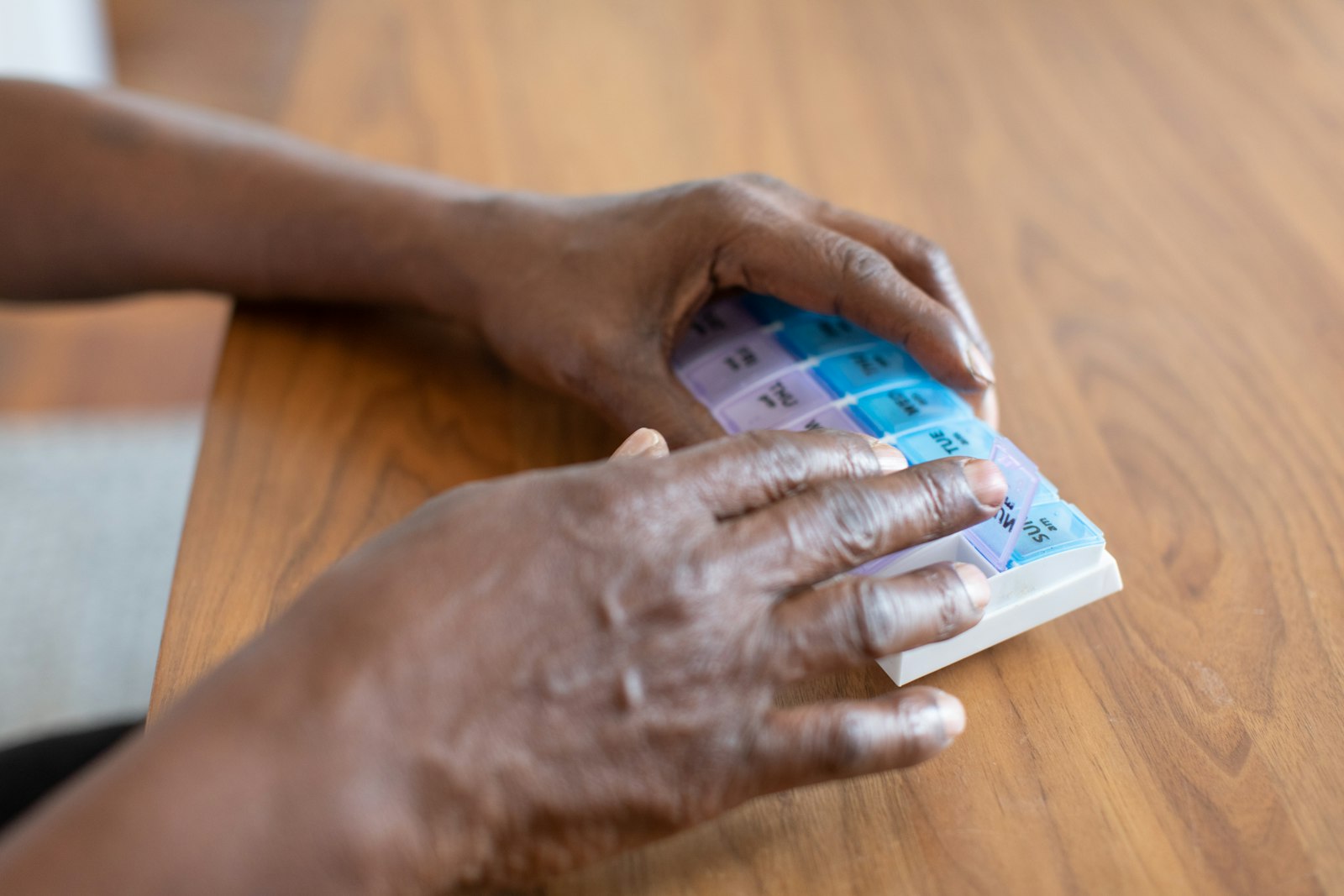 Two hands resting on a weekly pill organizer on a wooden table